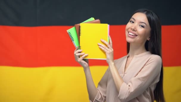 Perempuan ceria yang menunjukkan buku-buku salinan terhadap bendera Jerman, kursus bahasa asing — Stok Video