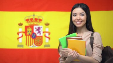 Neşeli Asyalı kız öğrenci İspanyol bayrağına karşı ayakta, dil eğitimi