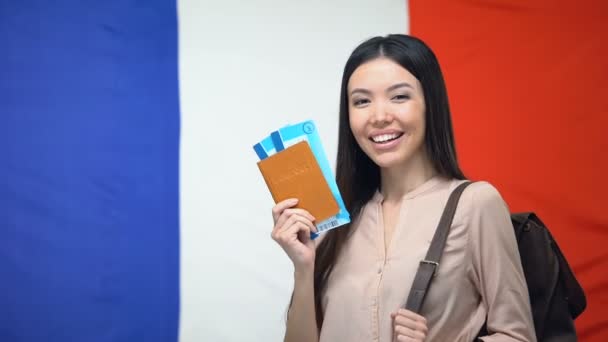 Mulher asiática feliz segurando passaporte e bilhetes de voo contra a bandeira francesa, viagem — Vídeo de Stock