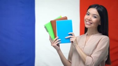 Gülümseyen Asyalı bayan Fransız bayrağı arka plan, dersler karşı copybooks gösteren