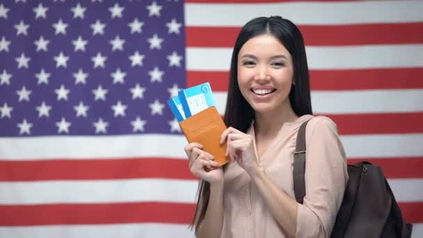 Mujer excitada sosteniendo pasaporte y billetes de avión contra fondo de bandera de EE.UU. — Vídeo de stock