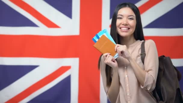 Feliz viajero femenino con pasaporte con billetes de avión contra bandera británica — Vídeos de Stock