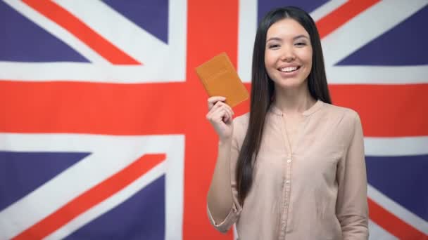 Sorridente ragazza asiatica in possesso di passaporto sullo sfondo bandiera britannica, cittadinanza — Video Stock