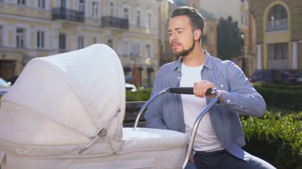 Martwi się młody ojciec stara się uspokoić noworodka swinging wózek w parku — Wideo stockowe