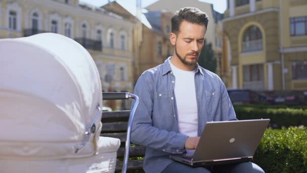 Modern young dad working laptop and swinging baby pram, multitasking lifestyle — Stock Video