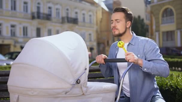 Jonge papa met rammelaar speelgoed swingende baby wandelwagen, goede vader, Kinderopvang, liefde — Stockvideo