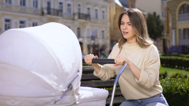 Bâillement mère balançant bébé chariot assis sur le banc du parc, manque de sommeil — Video