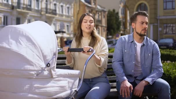 Upset mom worrying about crying baby pram, indifferent husband sitting on bench — Stock Video