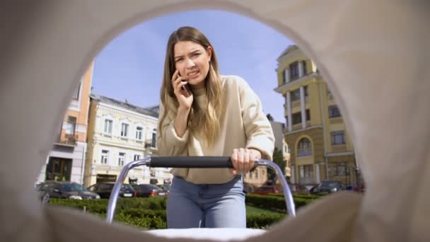 Ustaraná matka, mluvící telefon houpat dítě v kočárku, žádat o radu, POV — Stock video