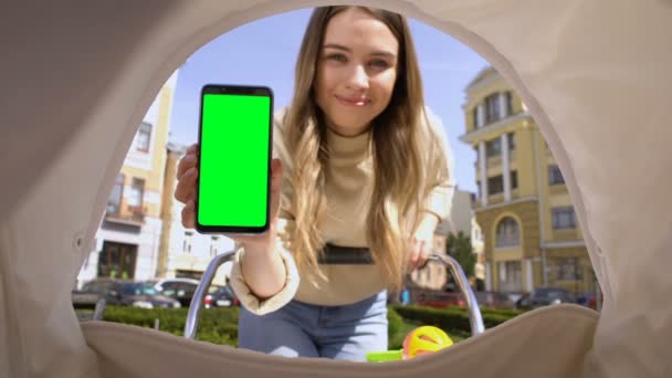 Mamma sorridente che mostra smartphone schermo verde al bambino in carrozza, applicazione ninna nanna — Video Stock