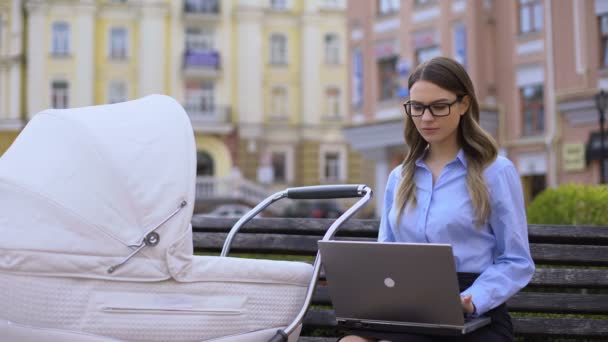Trabajadora de oficina preparando informe en laptop y cuidando recién nacido en cochecito — Vídeo de stock