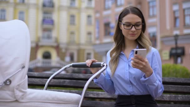 Joven madre en traje de oficina teléfono inteligente de trabajo y sonriendo al bebé en el carro — Vídeos de Stock