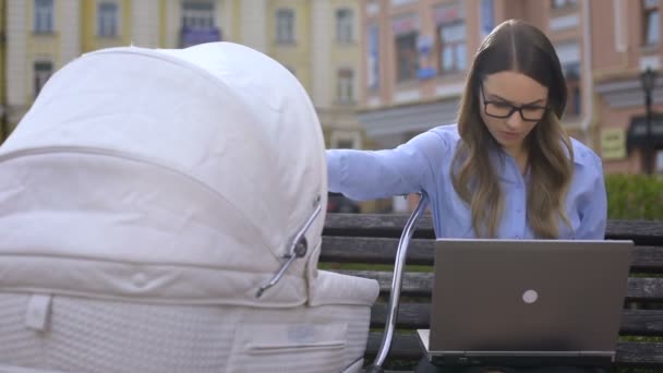 Employé de bureau occupé luttant contre le travail sur ordinateur portable et prenant soin du nourrisson en landau — Video