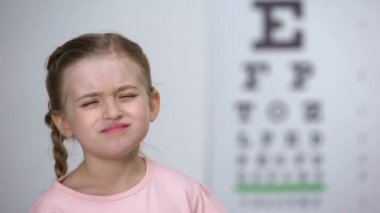 Küçük kız göz grafiğinden harfleri okumaya çalışıyor, yakın görüşlülük tanısı