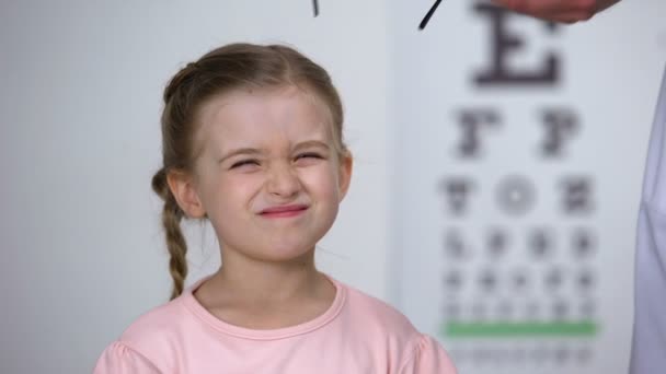 Оптик надевает очки на маленькую девочку и делает ее счастливой, профессиональной помощью — стоковое видео