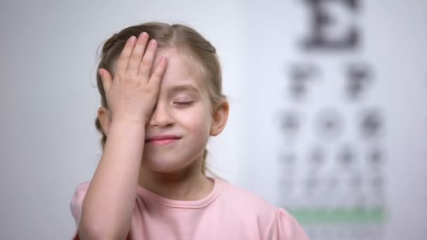 Ребенок закрывает глаза, показывает размер или знак из диаграммы глаза, диагностика зрения — стоковое видео