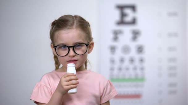 Веселый ребенок в очках пьет вкусный витаминный сироп, чтобы улучшить зрение — стоковое видео