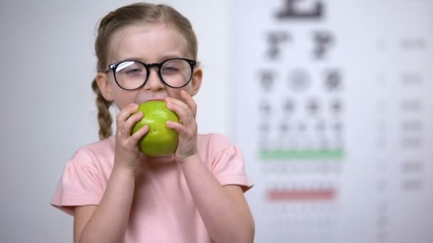 Menina adorável em óculos comer maçã, vitaminas naturais para os olhos, cuidados de saúde — Vídeo de Stock