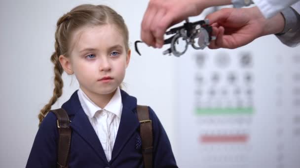 Оптометрист ставит оптическую рамку на школьницу, чтобы определить остроту зрения — стоковое видео