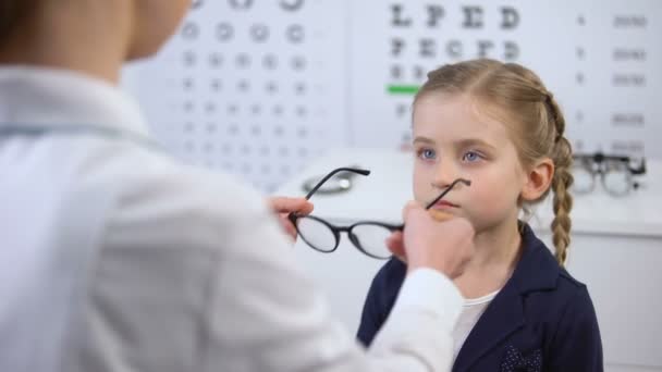 Female doctor putting glasses on disgruntled girl, child feels insecure, upset — Stock Video