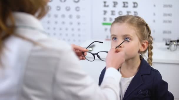 Happy little girl looking in mirror, choosing stylish glasses with doctor help — Stock Video