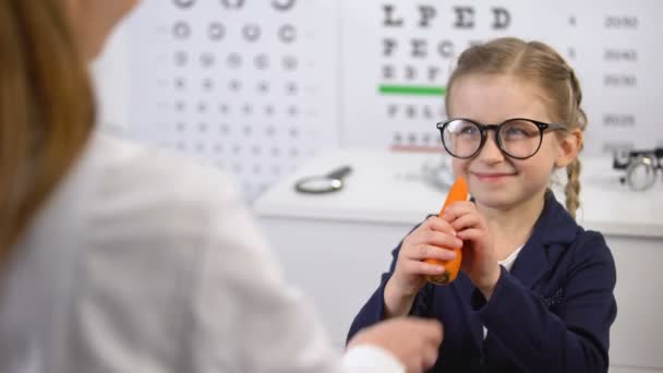 Optiker schenkt fröhlichem Kind Karotte, gesunde Vitaminnahrung für die Augen — Stockvideo