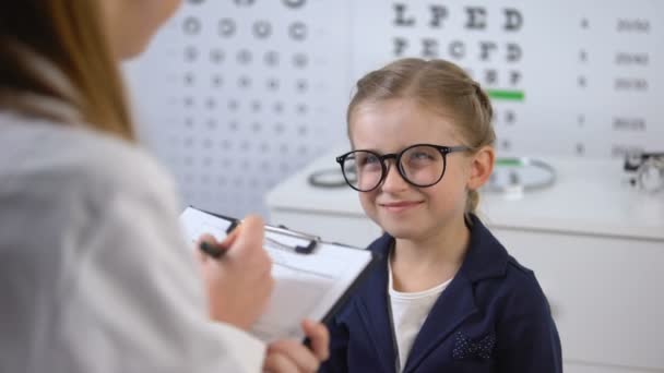 Śliczne uśmiechnięta dziewczyna czeka recepty okulary od optyka, porady leczenia — Wideo stockowe