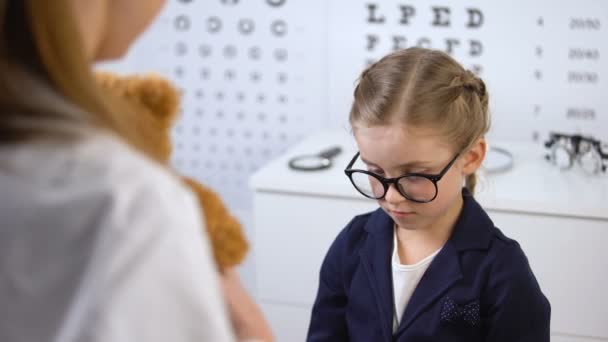 Kind optician giving teddy bear to upset child patient, psychological help — Stock Video