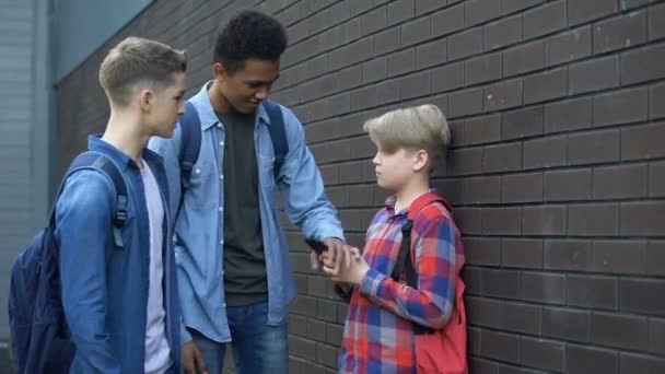 Старшокласники забирають телефон у молодшого, штовхаючого і глузуючого хлопчика, знущання — стокове відео