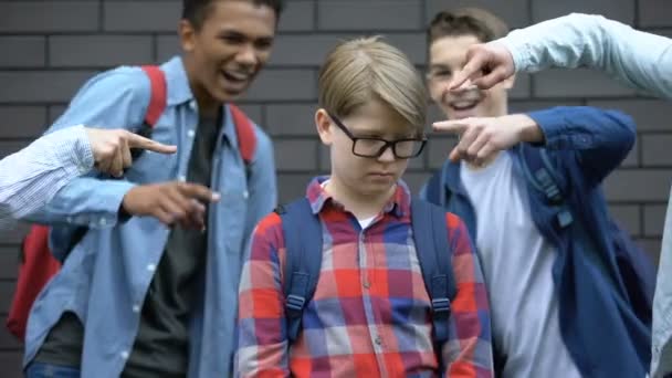 Schoolchildren wskazując palce u młodszego ucznia, szykanując inteligentnego chłopca, nękanie — Wideo stockowe