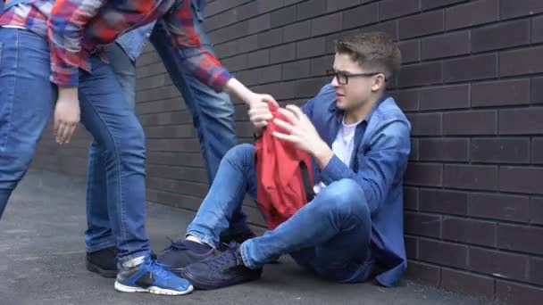 Estudiantes tirando cosas de la mochila en la cabeza de niño, acoso adolescente en la escuela — Vídeo de stock