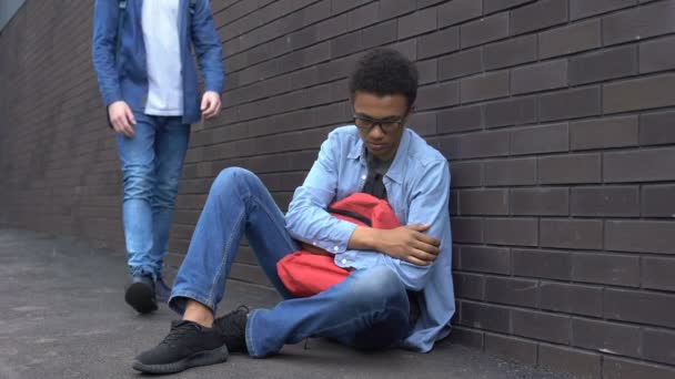 Подросток протягивает руку помощи запуганному афро-американскому мальчику, останавливает расизм — стоковое видео