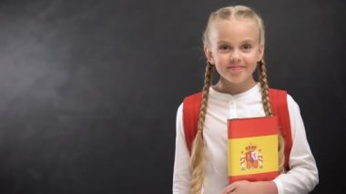 Gülümseyen kız öğrenci kara tahta arka plan karşı İspanyolca dil kitabı tutan
