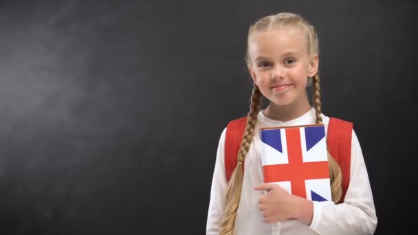Усміхнені жінка-учень тримає підручник з надрукованим прапором Великої Британії, мов — стокове відео