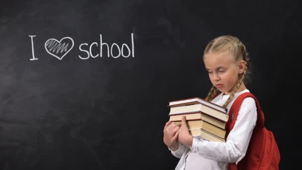 Freche Schulmädchen mit Büchern, die neben der Tafel stehen, ich liebe die Schule geschrieben — Stockvideo