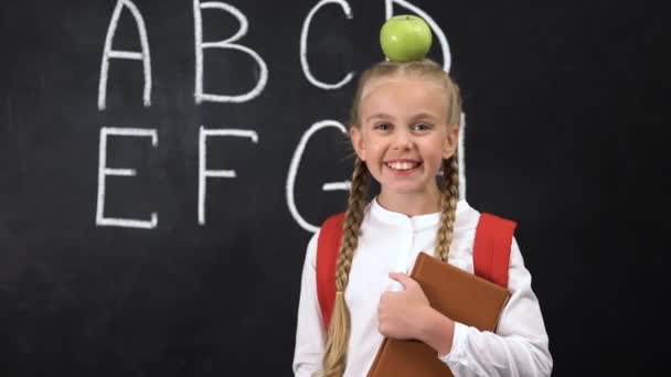 Όμορφη μαθήτρια στέκεται κοντά στον μαυροπίνακα με το μήλο στο κεφάλι, λαμπρή ιδέα — Αρχείο Βίντεο