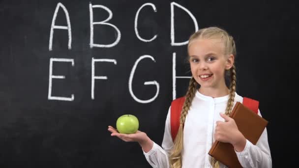 Niña sosteniendo manzana cerca de pizarra, bocadillos saludables para niños, alfabeto escrito — Vídeos de Stock