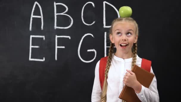 Очаровательная школьница, стоящая с яблоком на голове, имея хорошую идею, умный ребенок — стоковое видео