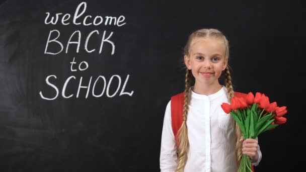 Cute smiling girl holding bunch of tulips near chalkboard welcome back to school — Stock Video