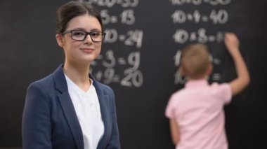 Genç kadın öğretmen kamera bakıyor, matematik egzersizleri çözme okul çocuğu, iş