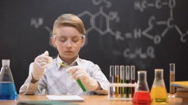 Koruyucu gözlüklü çocuk tüpe kimyasal madde döküyor, reaksiyonu kontrol ediyor