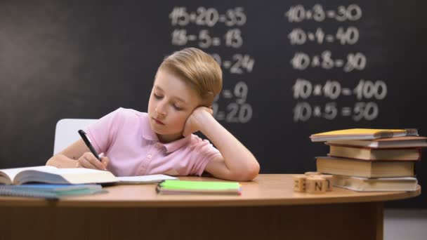 Розслаблений нудний школяр сидить за столом, не бажаючи готувати математичне домашнє завдання — стокове відео