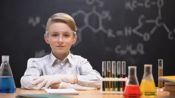 Piccolo genio seduto in occhiali protettivi, liquidi chimici in tubi sul tavolo — Video Stock