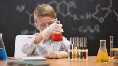 Okul çocuğu şişede tortu ya bakıyor ve sonuç yazıyor, kimya dersi