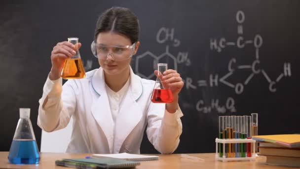 Química feminina mostrando líquidos em frascos para câmera, desenvolvendo nova substância — Vídeo de Stock