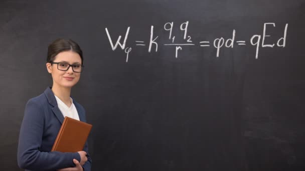 Jeune professeur intelligent debout près du tableau noir et regardant à la caméra, formule — Video