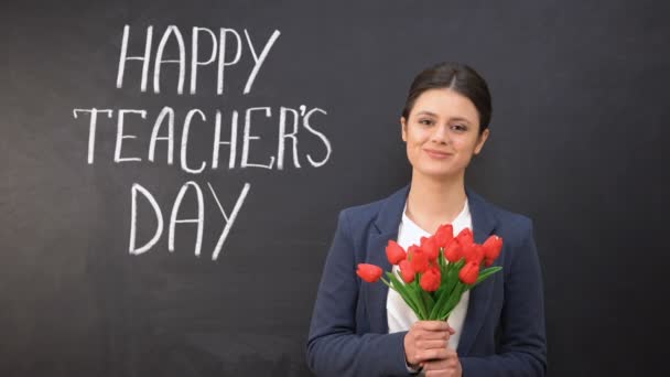 Χαρούμενη μέρα δασκάλων γραμμένη στον μαυροπίνακα, χαμογελαστή Κυρία με τουλίπες που στέκονται κοντά — Αρχείο Βίντεο