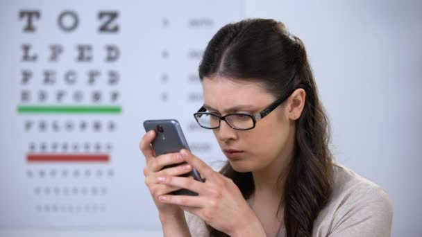 Frau mit Brille tippt auf Smartphone, moderne Technologien, kleine Schrift — Stockvideo