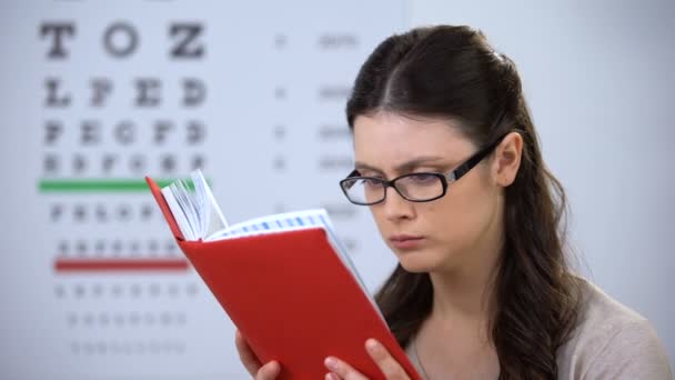 眼鏡の女性は、近視読書本を苦しんで、正しいレンズディオプターの必要性 — ストック動画