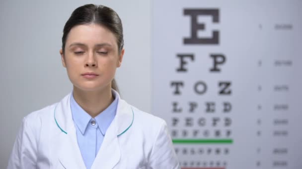 Дружелюбная женщина-оптометрист показывает бутылку с витаминами для поддержания зрения — стоковое видео